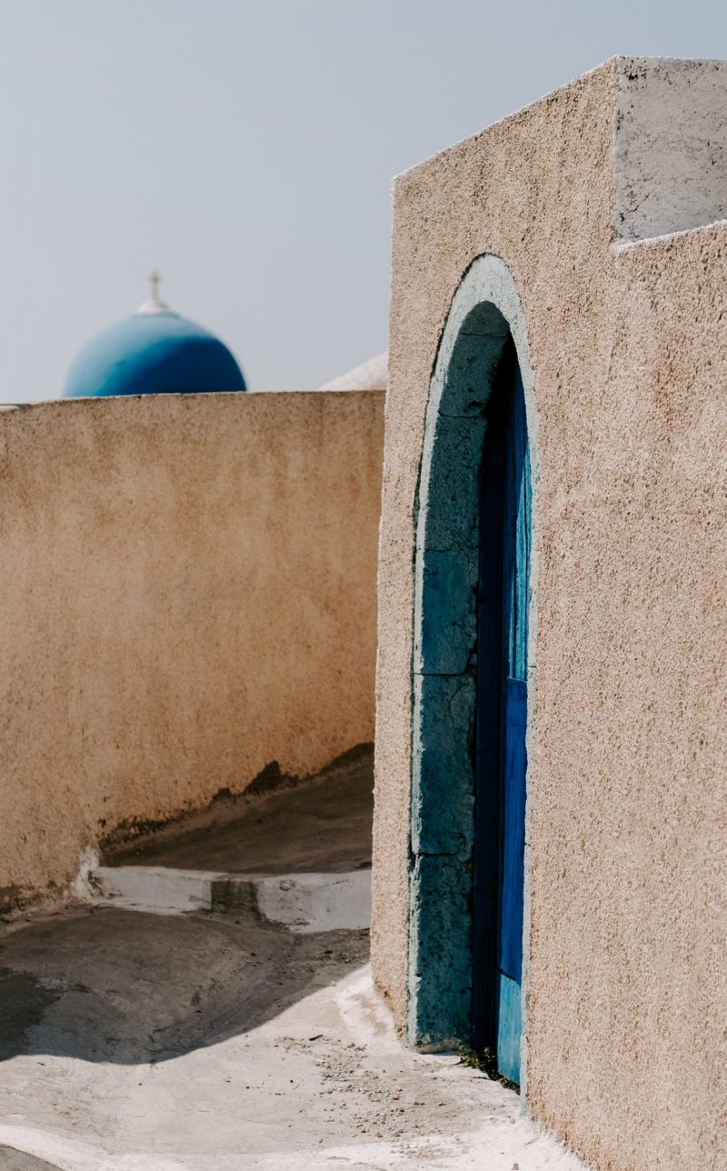 An artistic snapshot from an alley in Santorini with a dome in the background