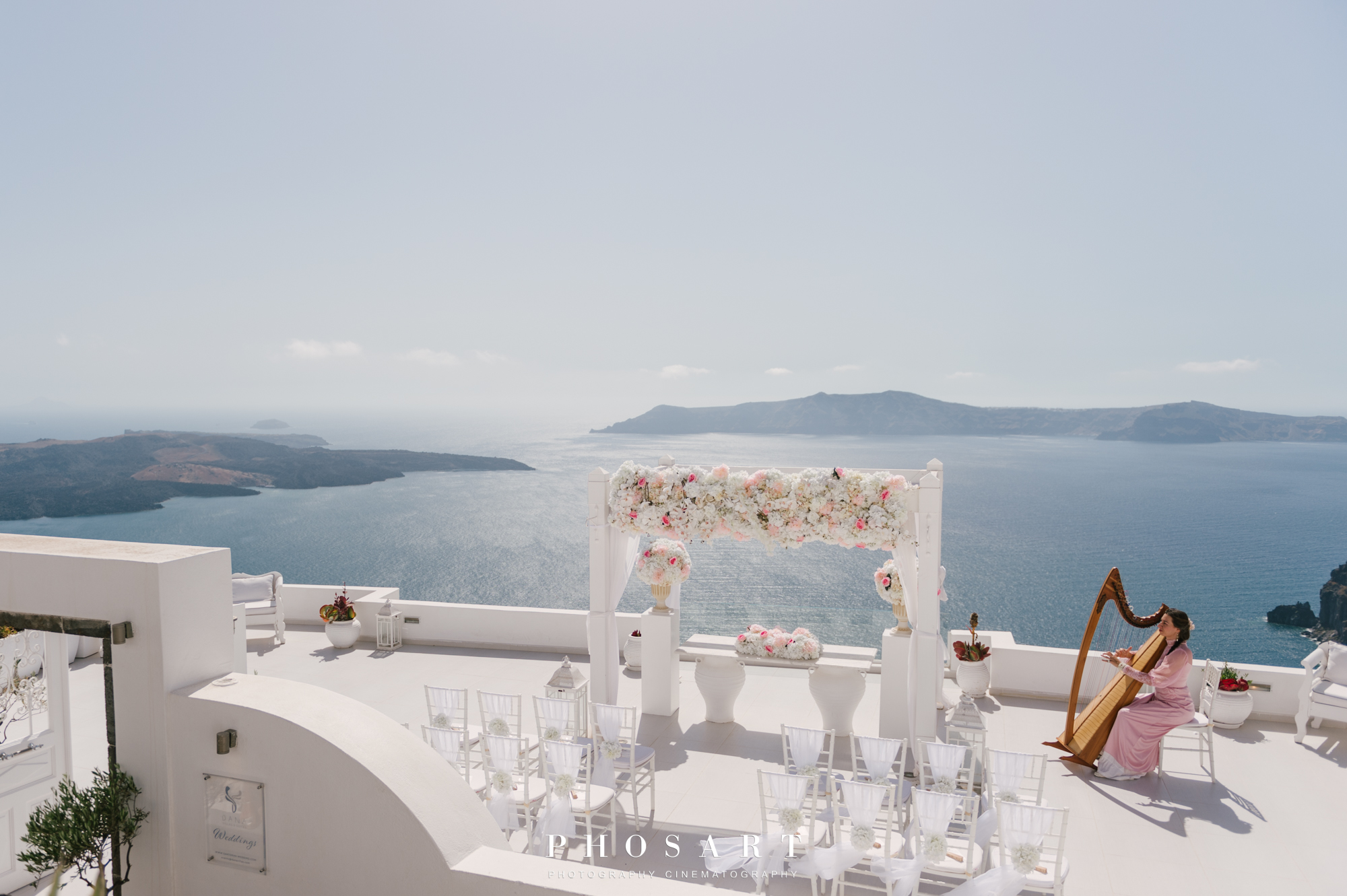 Dana Villas' large terrace above the caldera decorated with white furniture and flowers for a wedding ceremony