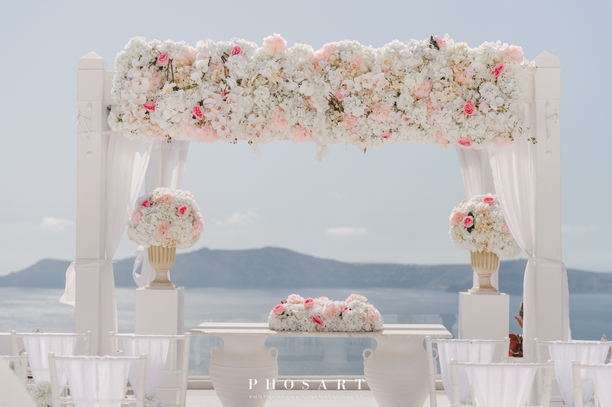 a white wooden kiosk overlooking the Aegean, decorated with white flowers and wooden white empty chairs before the wedding ceremony
