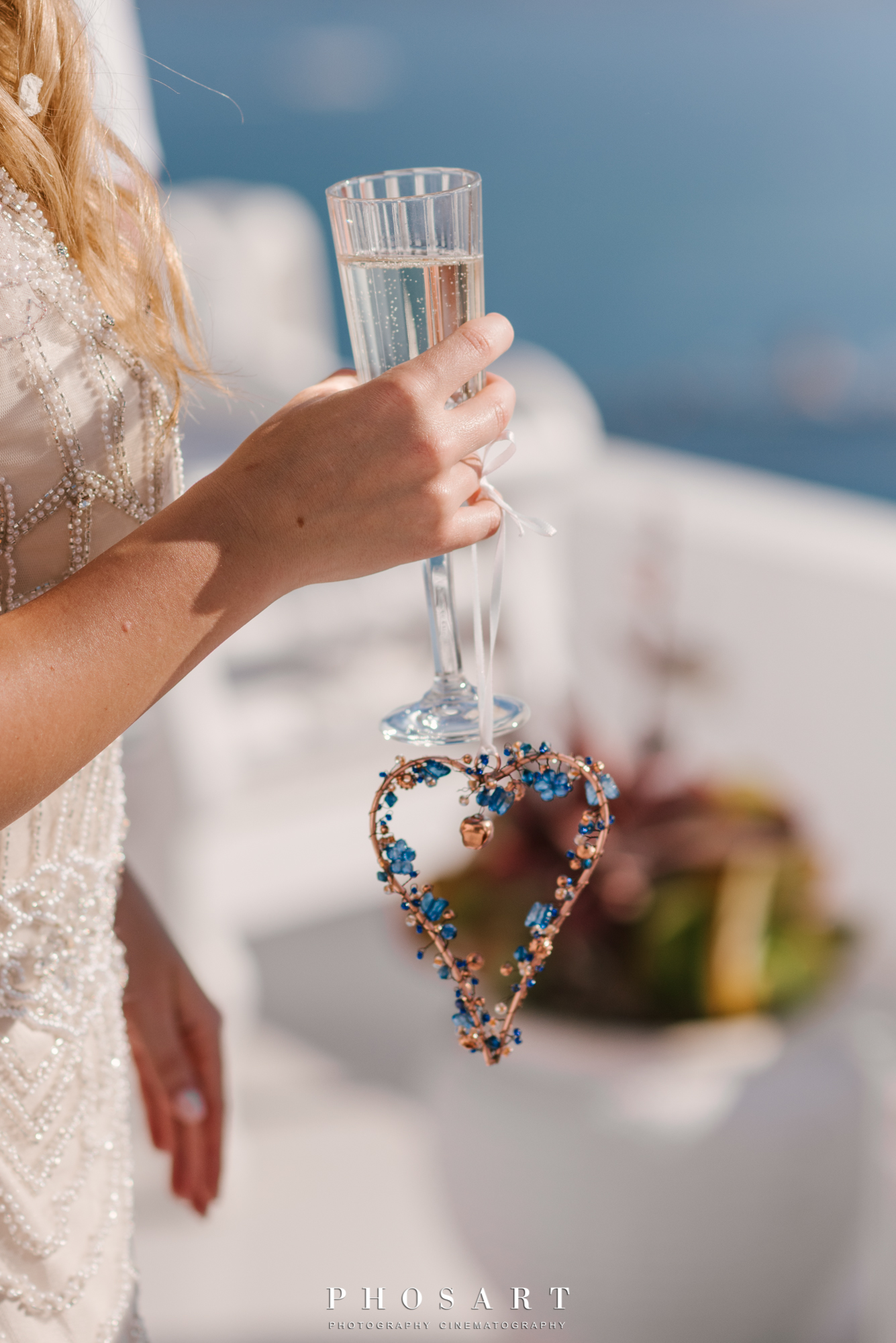 Bride holds a glass of champagne adorned with a heart made of wire and blue stones