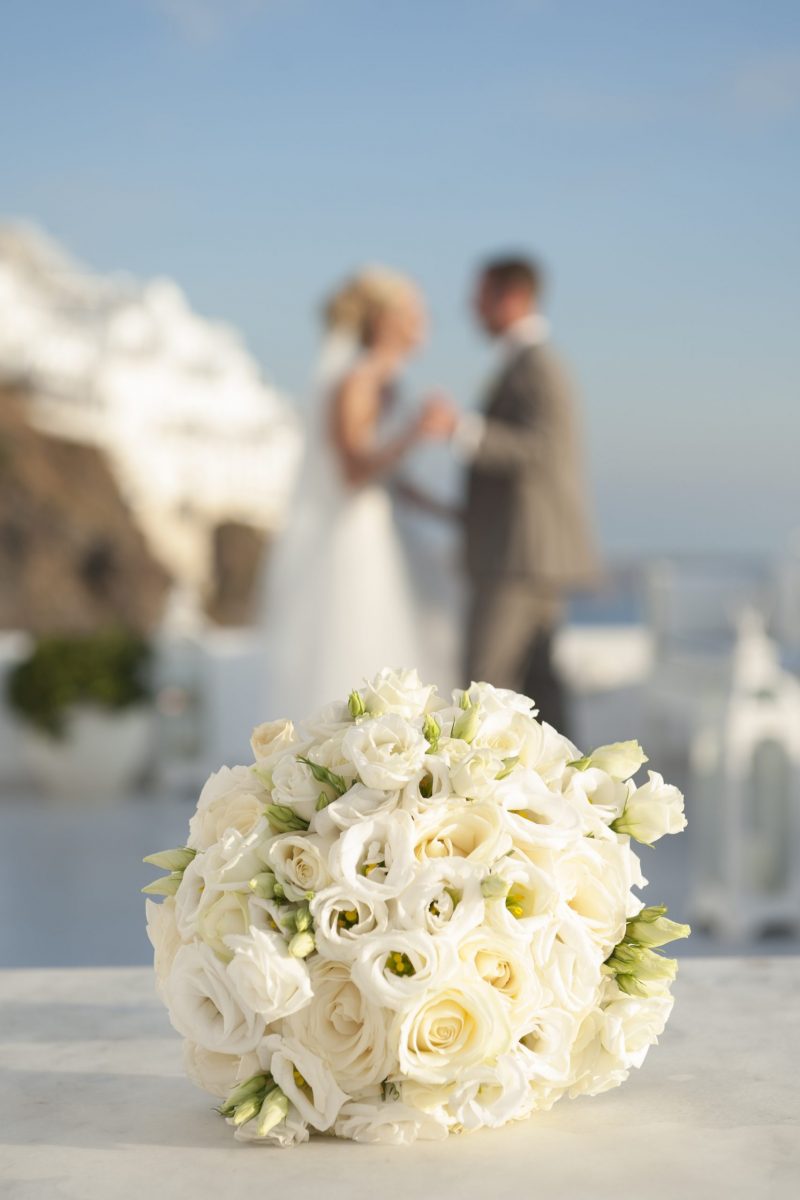 A bridal bouquet of white roses and the blurred figure of a couple on the backround