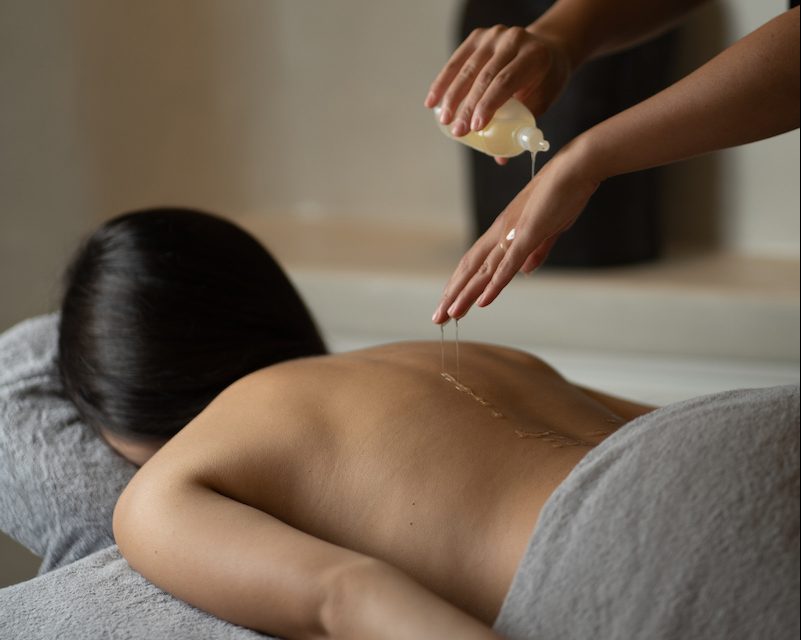 Dana Villas Soma Spa specialist pours oil on woman's back during massage treatment