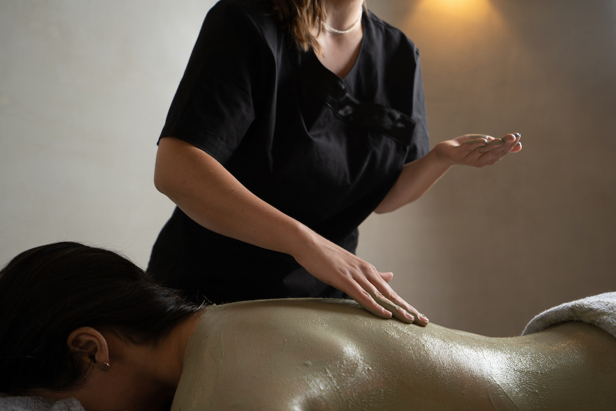 Dana Villas Soma spa specialist spreads clay on woman's body during beauty and rejuvenation treatment